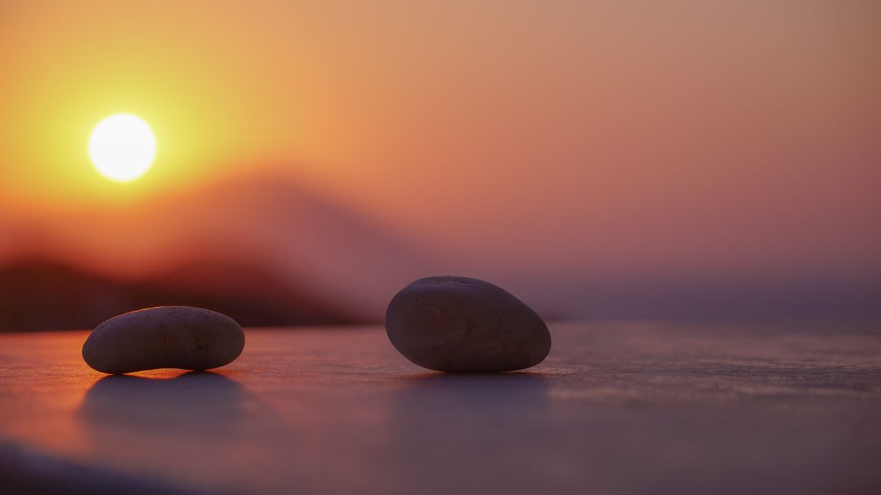 Ground level of stones on sandy shore near ocean behind mountains under bright sky with shining sun in twilight